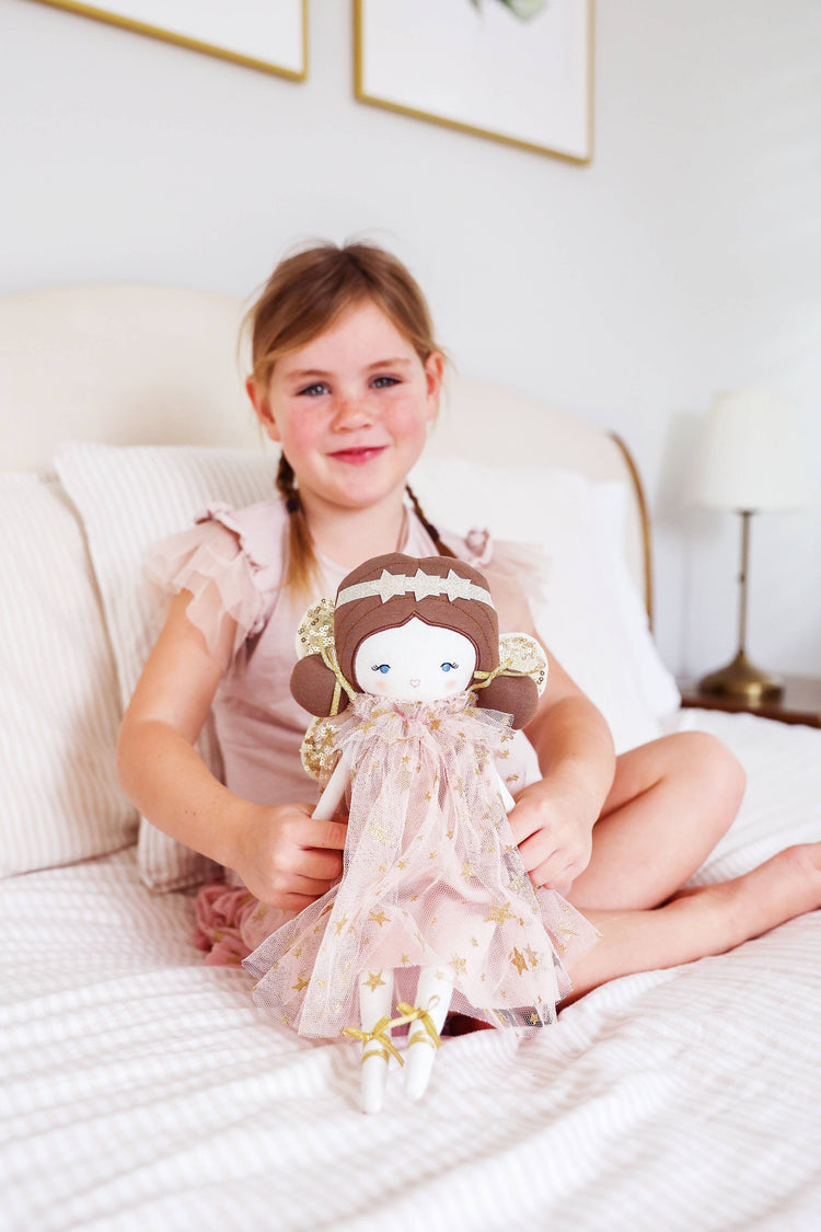 Girl sitting on bed holding dolly dressed with headband 