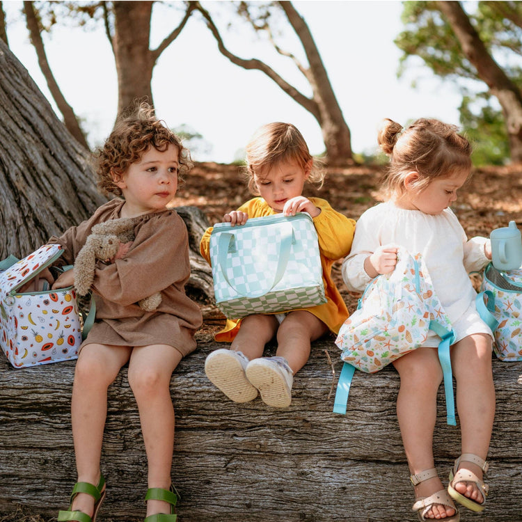 Children holding IZImini lunch bags sitting in a park. 